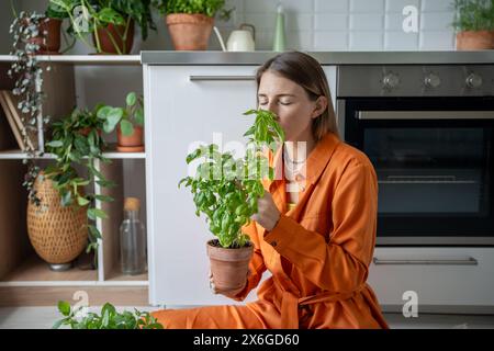 Femme appréciant l'odeur du basilic. La fille est assise sur le sol, inspire l'arôme du basilic cultivé maison dans le pot Banque D'Images