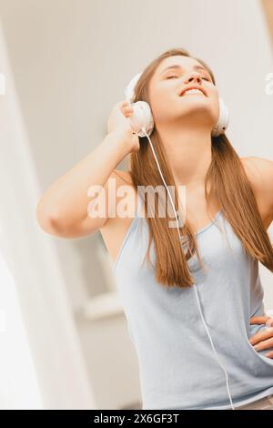 Jeune femme rayonnante aime la musique sur son casque blanc, son visage illuminé d'un sourire joyeux dans une pièce ensoleillée Banque D'Images