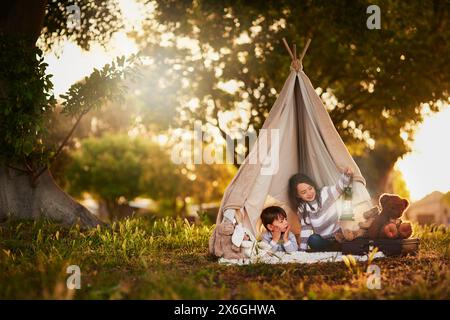 Tipi, enfants et jouer dans la tente de jardin en plein air dans la nature pour le camping, le plaisir et l'aventure avec imagination. Tissu, lumière et maison fantaisie pour les enfants Banque D'Images