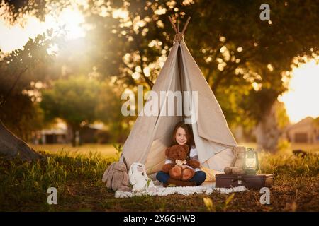 Tipi, tente et fille avec jouet dans le jardin dans la nature pour le plaisir, le jeu et le camping pour l'aventure ou l'imagination. Tissu, abri ou maison de fantaisie pour Banque D'Images