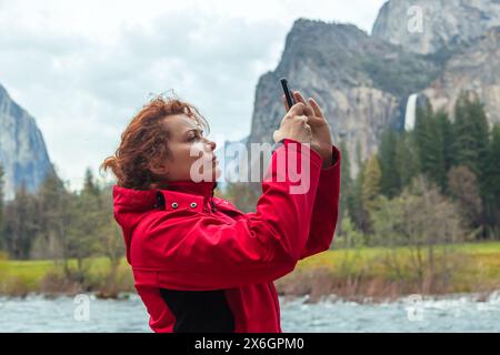 Jeune femme prend des photos d'un paysage naturel dans Yosemite Park, Californie avec un appareil photo de smartphone. Yosemite Falls au printemps. Vue panoramique sur les montagnes rocheuses contre le ciel Banque D'Images