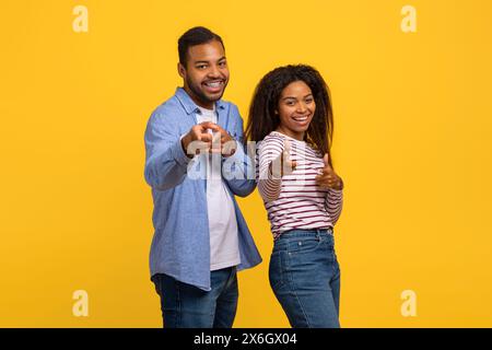 Couple heureux pointant vers caméra sur un fond jaune vif Banque D'Images