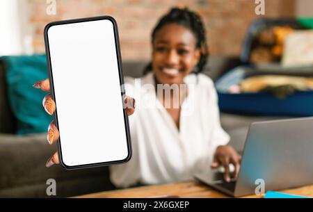 Femme noire tenant le téléphone portable devant l'ordinateur portable Banque D'Images