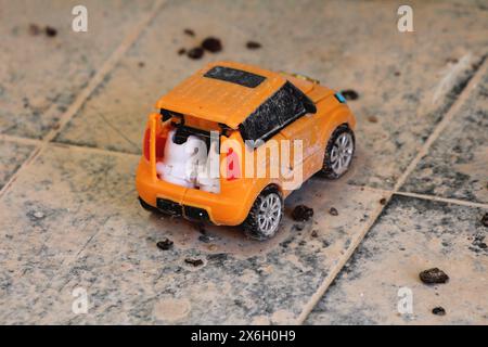 Sale vieille voiture rétro rétro vintage orange enfants jouet voiture laissée sur des carreaux de céramique noire recouverts de sable et de poussière dans la salle de bains de la maison de famille abandonnée Banque D'Images