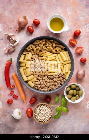 Poêle avec des pâtes italiennes mélangées et une variété de légumes sur un fond texturé Banque D'Images