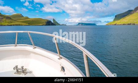 Vue sur le bateau touristique croisière dans les fjords des îles Féroé au ciel bleu et jour ensoleillé. Banque D'Images