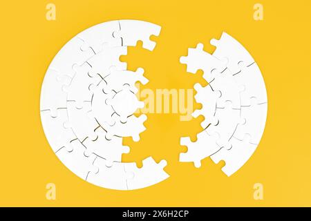 Vue de dessus d'un puzzle circulaire blanc divisé en deux parties sur un fond jaune. Banque D'Images