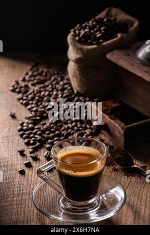 En arrière-plan, des grains de café et du café moulu, au premier plan un espresso dans une tasse en verre Banque D'Images