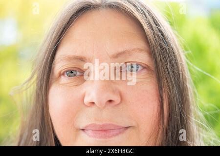 Femme attirante de 50 ans positive caucasienne regardant la caméra, joli portrait du visage en gros plan, rides sur la peau, lifting du visage, changements cutanés liés à l'âge Banque D'Images