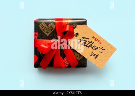 Bonne fête des pères. Vue de dessus de la boîte-cadeau avec l'arc rouge et l'étiquette de vente brune avec le texte Happy Father's Day sur fond bleu Banque D'Images