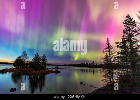 Les aurores boréales éclatent au-dessus d'un lac du Minnesota dans un ciel sombre au-dessus de l'arc-en-ciel brillant de lumière aurore alors que le soleil se couche sur l'horizon Banque D'Images