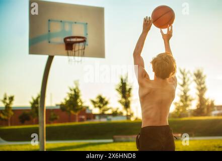 Enfant garçon jouant au basket-ball vue de dos sur le coucher du soleil Banque D'Images