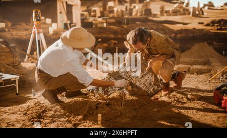 Site de fouille archéologique : deux grands archéologues travaillent sur le site de fouille, nettoyant soigneusement, soulevant des artefacts culturels de civilisation ancienne nouvellement découverts, tablette d'argile historique, restes fossiles Banque D'Images