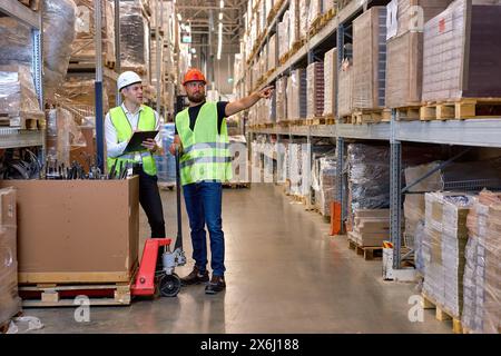 deux gestionnaires d'entrepôt marchant dans un grand centre de distribution d'entrepôt discutant de l'augmentation de la productivité. bon travail d'équipe, des hommes habillés en wor Banque D'Images