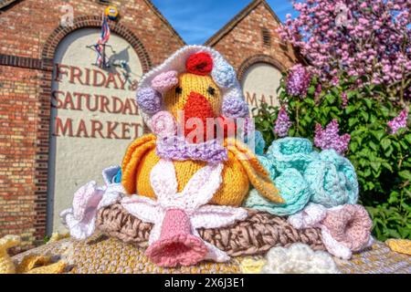 Topper coloré de boîte postale tricoté d'un canard jaune vif avec un bonnet tricoté entouré de fleurs devant le centre-ville de Malthouse Hythe Banque D'Images