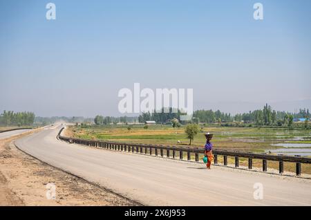 Budgam, Inde. 15 mai 2024. Une femme marche le long d'une autoroute en construction par une journée ensoleillée. (Photo par Idrees Abbas/SOPA images/SIPA USA) crédit : SIPA USA/Alamy Live News Banque D'Images