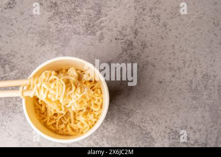 Vue aérienne d'un bol de soupe de pâtes instantanées avec une paire de chopstickson un fond gris clair. Déjeuner. Concept de restauration rapide Banque D'Images