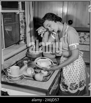 Rétro femme au foyer pose la vaisselle épuisée, mettant sa main sur son front dans une photo promotionnelle exagérée, une femme au foyer et ses tâches domestiques. Amérique États-Unis Banque D'Images