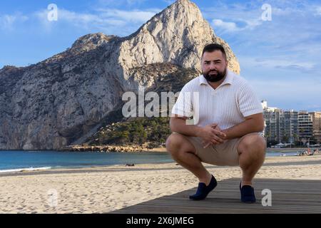 Cette image évocatrice capture un homme de 30 ans dans un moment de réflexion, avec le majestueux Ifach Rock se levant en arrière-plan. Banque D'Images