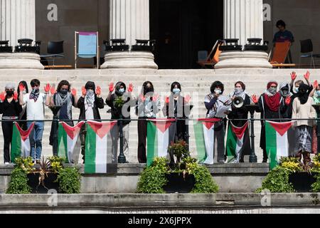 Londres, Royaume-Uni. 15 mai 2024. Des étudiants avec des mains peintes en rouge se tiennent derrière une rangée de drapeaux palestiniens sur les marches de l'University College de Londres alors que 'UCL signifie Justice' rallie dans l'enceinte de l'université, qu'ils occupent depuis le 2 mai 2024, pour protester contre la guerre d'Israël contre Gaza et exiger que le collège se désengage des entreprises, y compris des fabricants d'armes, qui approvisionnent Israël et appeler l'université à condamner les actions israéliennes qui violent le droit international. L'occupation étudiante est l'une des nombreuses qui se déroulent dans le centre de Londres. Crédit : Ron Fassbender/Alamy Live News Banque D'Images