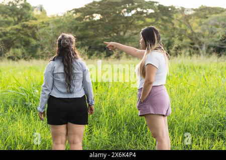 Deux jeunes femmes latines dans un champ d'herbes hautes, on pointe de sa main quelque chose qu'elle veut montrer à son amie Banque D'Images