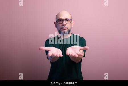 Homme chauve barbu avec des lunettes de vue montrant sa paume. Isolé sur fond de couleur saumon. Banque D'Images