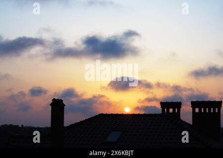 Cheminées, toit en tuiles d'une maison et beaux nuages dans la brume au coucher du soleil Banque D'Images