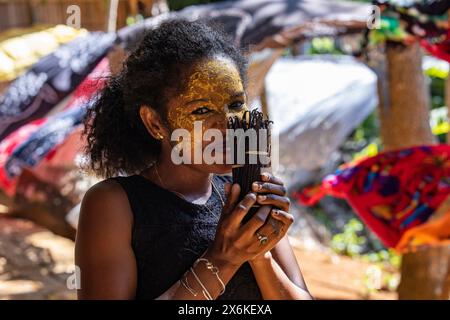Femme heureuse avec la peinture visage Masonjoany comme crème solaire sent les haricots de vanille à vendre au marché local, Nosy Komba, Diana, Madagascar, Océan Indien Banque D'Images