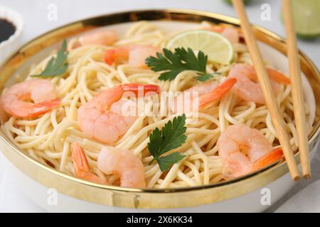 Savoureux spaghetti aux crevettes, citron vert et persil dans un bol sur une table blanche, gros plan Banque D'Images