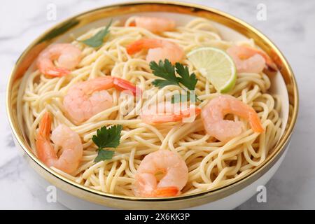 Savoureux spaghetti aux crevettes, citron vert et persil dans un bol sur une table blanche, gros plan Banque D'Images