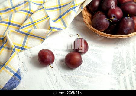 Prunes d'été juteuses. Plusieurs prunes douces mûres sur fond de bois blanc avec serviette de cuisine bleue. Banque D'Images