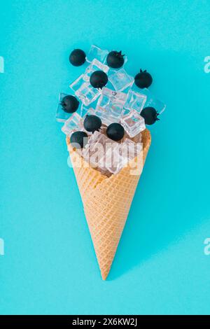 Cône de crème glacée avec des myrtilles et des glaçons sur fond bleu aqua. Aménagement créatif estival minimal. Concept de fruits et bonbons. aest de nourriture sucrée estivale Banque D'Images