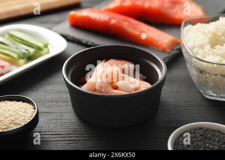 Crevettes dans un bol et d'autres ingrédients pour sushi sur une table en bois noir, gros plan Banque D'Images