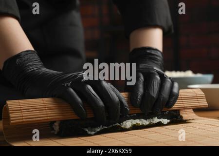 Chef en gants faisant rouler des sushis à la table en bois, gros plan Banque D'Images