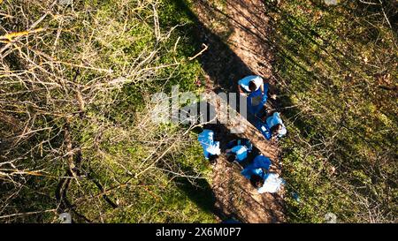 Tir par drone d'une équipe d'activistes nettoyant et recyclant les ordures dans une forêt, travaillant à défricher la zone boisée pour la protection de l'environnement. Personnes ayant des valeurs de préservation écologique. Banque D'Images