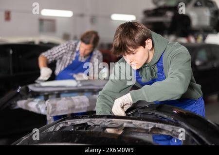 Le jeune mécanicien répare une pièce de voiture Banque D'Images