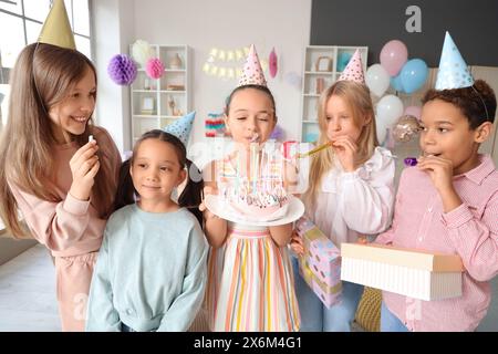 Mignonne petite fille soufflant des bougies sur le gâteau d'anniversaire avec ses amis à la fête à la maison Banque D'Images