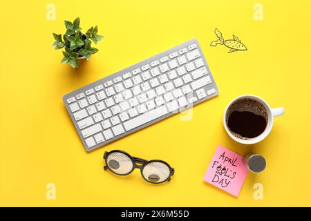 Clavier d'ordinateur, note collante, sel et tasse de café sur fond jaune. Farce du jour des fous d'avril Banque D'Images