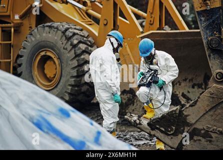 Deux travailleurs portant des combinaisons et des masques de protection contre les matières dangereuses examinant des échantillons de terre polluée sur un site EPA superfund Banque D'Images