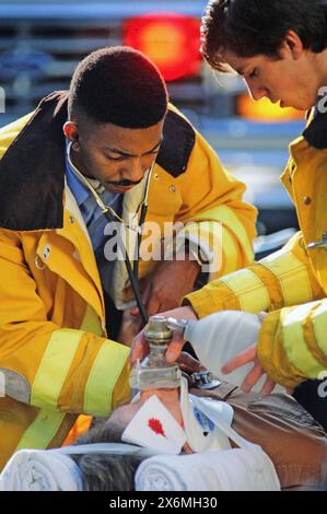 Deux ambulanciers paramédicaux dévoués en gilets jaunes fournissent une assistance médicale urgente à une personne blessée dans la rue. Utilisation d'un stéthoscope et d'autres ess Banque D'Images