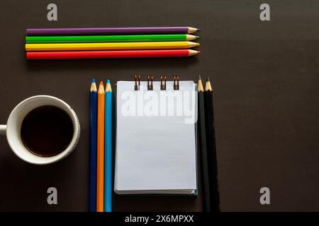 Crayons colorés alignés à côté d'un bloc-notes sur un bureau sombre Banque D'Images