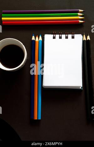 Crayons colorés alignés à côté d'un bloc-notes sur un bureau sombre Banque D'Images