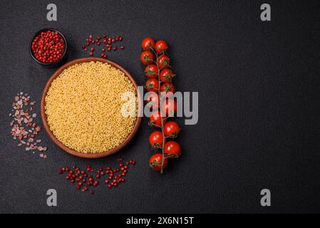 Pâtes anellini crues de blé dur avec du sel et des épices sur un fond de béton foncé Banque D'Images