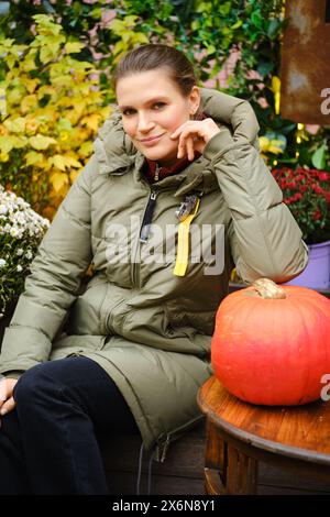 Femme mi-âge souriante en veste chaude en duvet parmi la décoration d'automne Banque D'Images