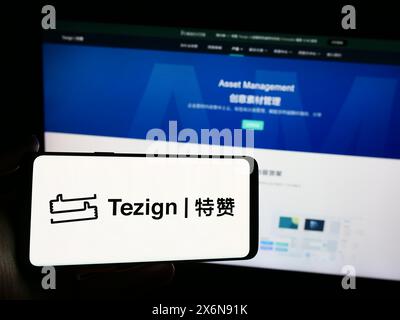 Personne tenant un smartphone avec le logo de la société chinoise d'analyse de contenu Tezign en face du site Web. Concentrez-vous sur l'affichage du téléphone. Banque D'Images