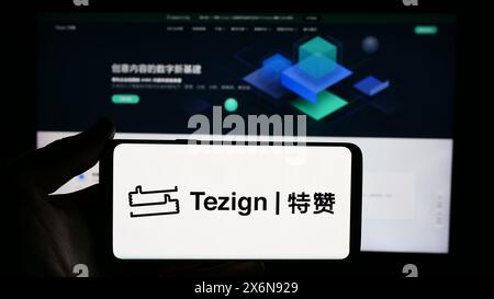 Personne tenant le téléphone portable avec le logo de la société chinoise d'analyse de contenu Tezign devant la page Web de l'entreprise. Concentrez-vous sur l'affichage du téléphone. Banque D'Images