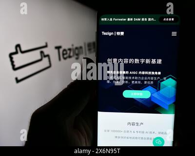 Personne tenant un smartphone avec le site Web de la société chinoise d'analyse de contenu Tezign devant le logo de l'entreprise. Concentrez-vous sur le centre de l'écran du téléphone. Banque D'Images