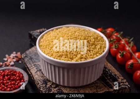 Pâtes anellini crues de blé dur avec du sel et des épices sur un fond de béton foncé Banque D'Images