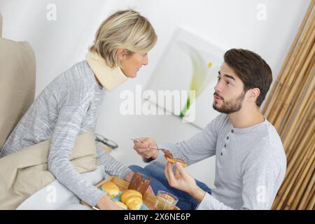 jeune homme servant de la nourriture à une femme blessée au lit Banque D'Images