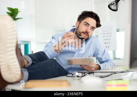 homme mangeant dans le lieu de travail avec les pieds sur le bureau Banque D'Images